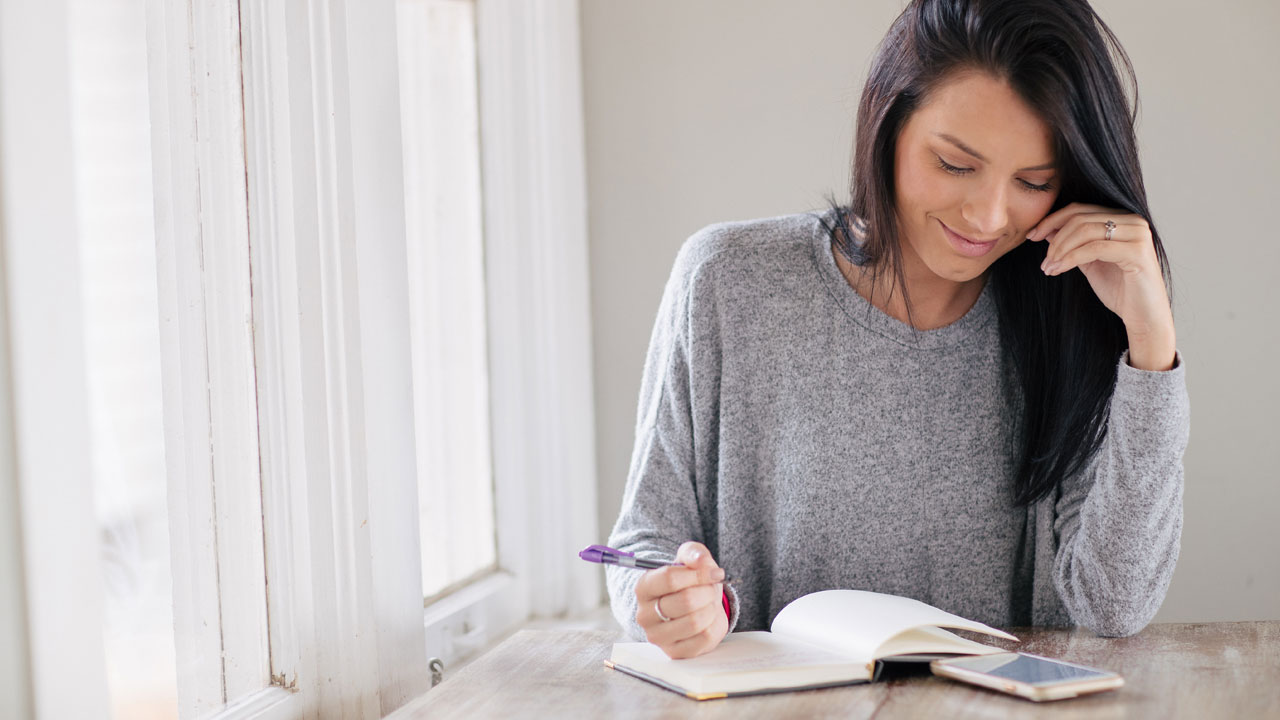 Woman journaling while reading the Bible on her phone